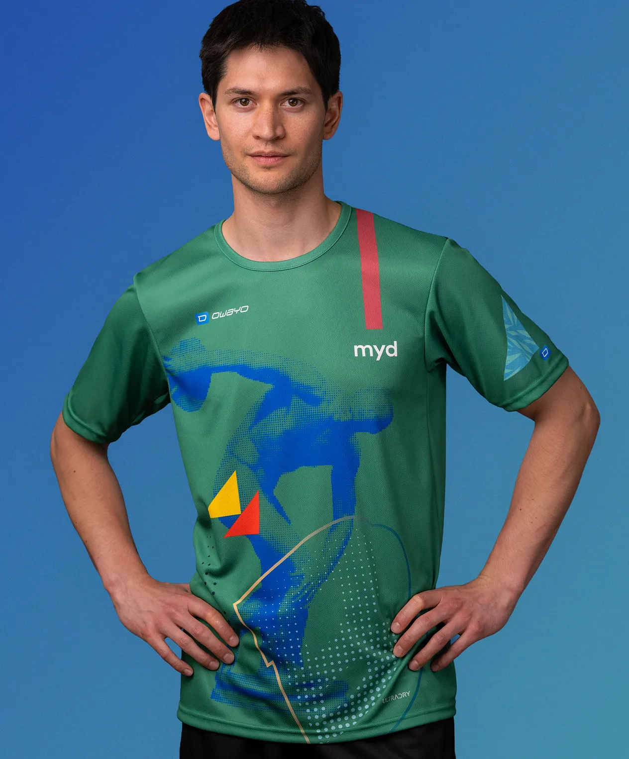 Ein Mann in einem grünen, maßgeschneiderten Sporttrikot von owayo mit einem blauen, gelben und roten grafischen Design und der Aufschrift 'myd' auf der Brust.